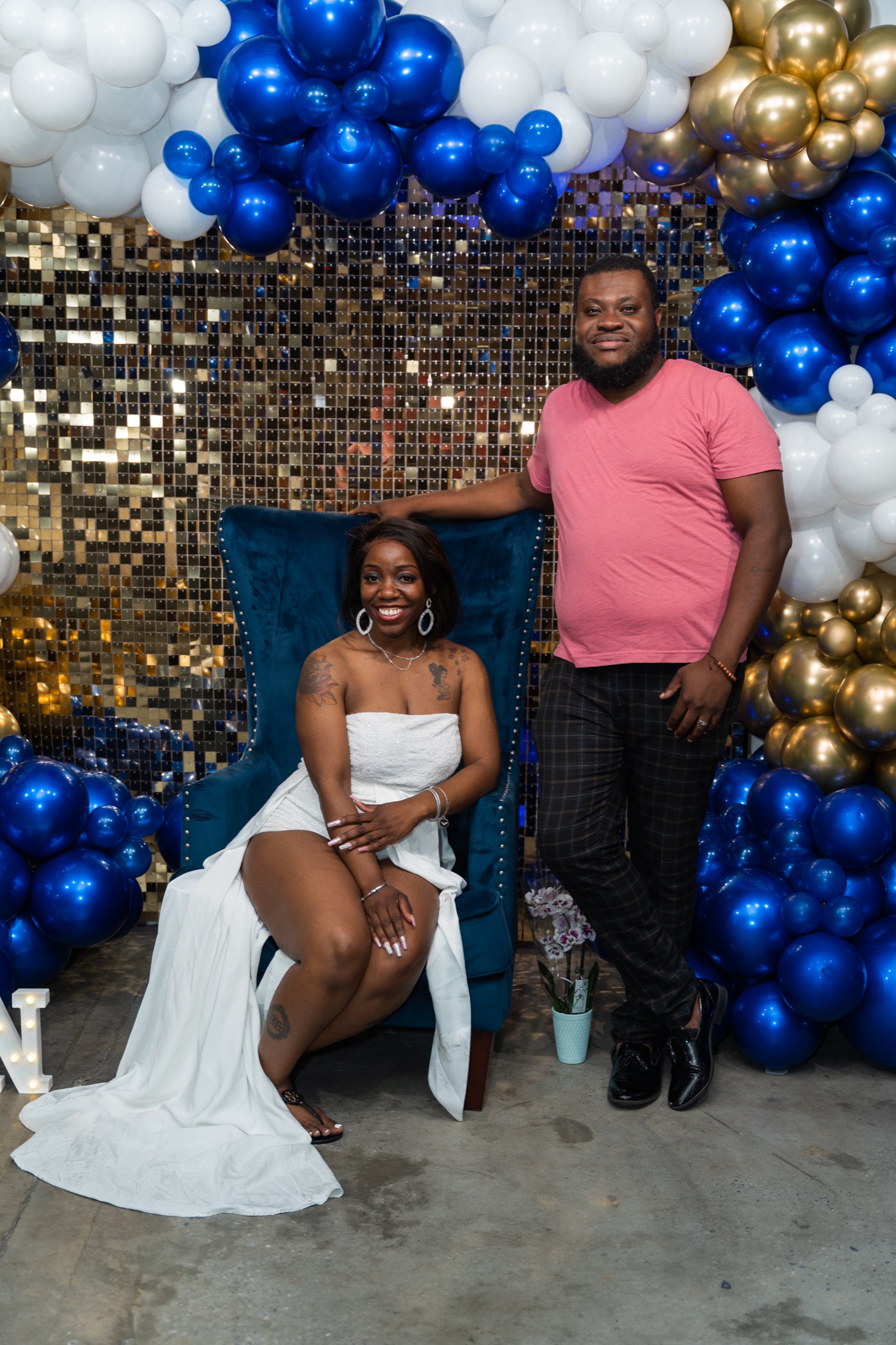 A couple celebrating together in front of a blue, white and gold balloon display
